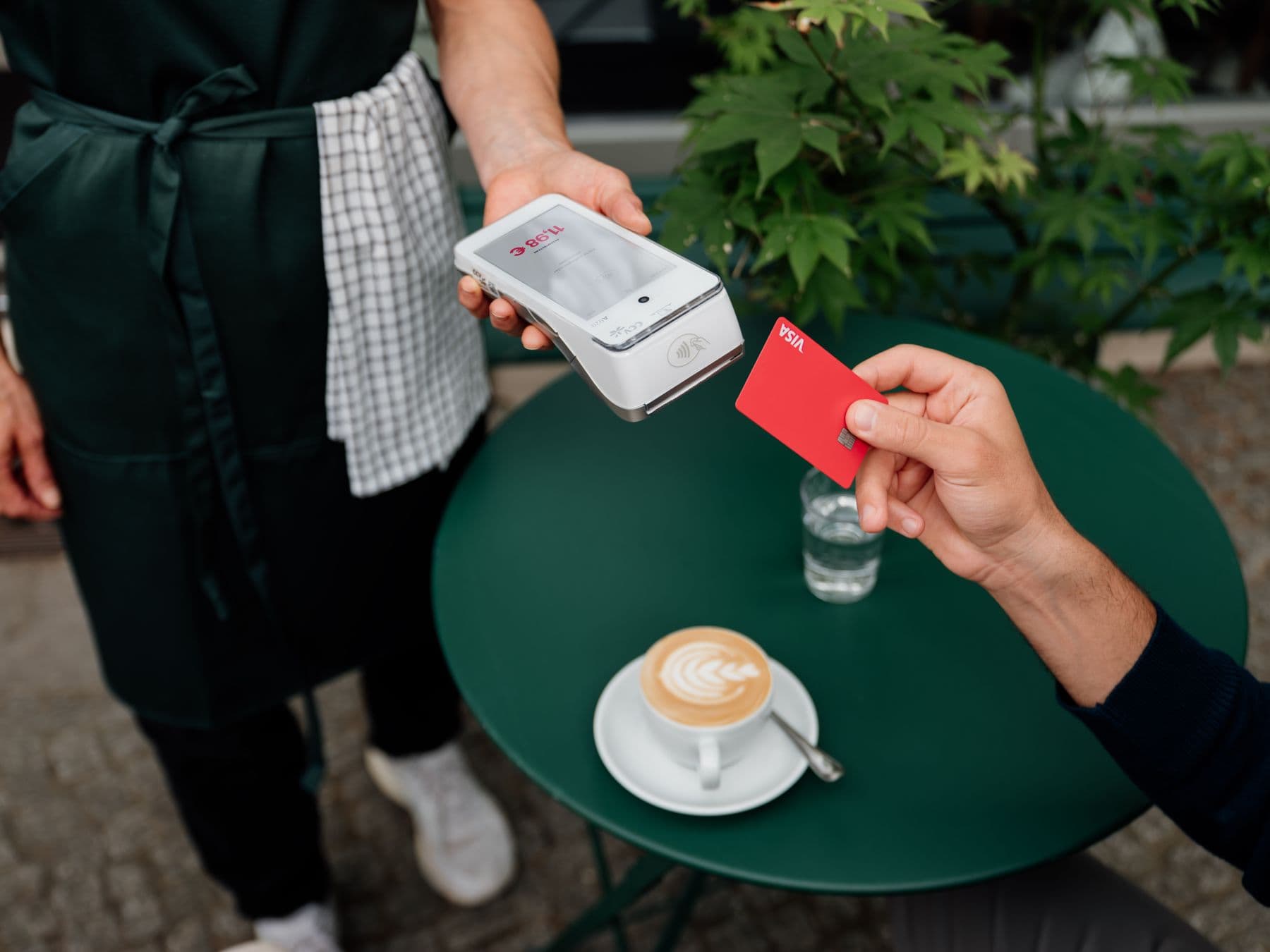 A guest pays by card on a POS terminal at a terrace table